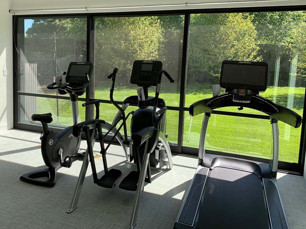 Home gym with premium, commercial-grade exercise bike, Arc Trainer, and treadmill facing window