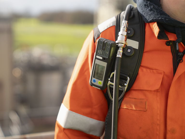 Worker in an orange safety jacket with Draeger Gas Detection equipment.