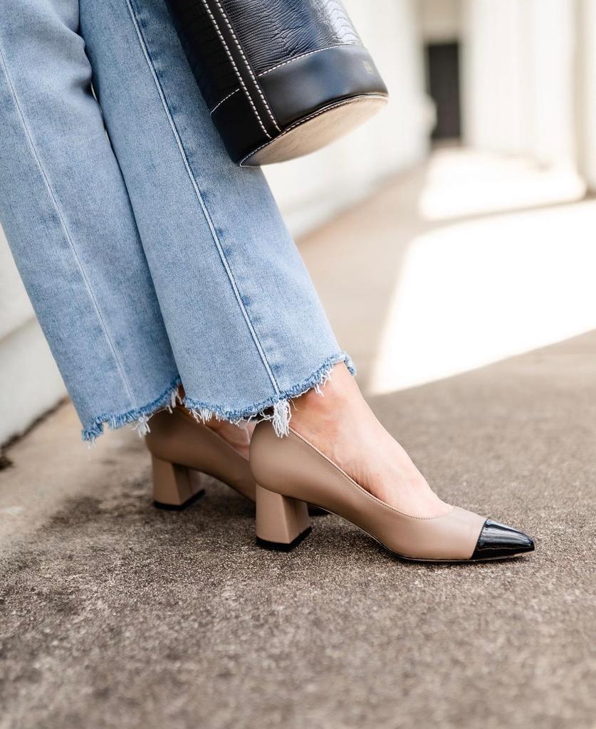 A person wearing beige and black high-heeled shoes with frayed jeans.