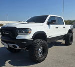 Front view of lifted white RAM 1500 Rebel with Nitto Mud Grappler tires and custom wheels