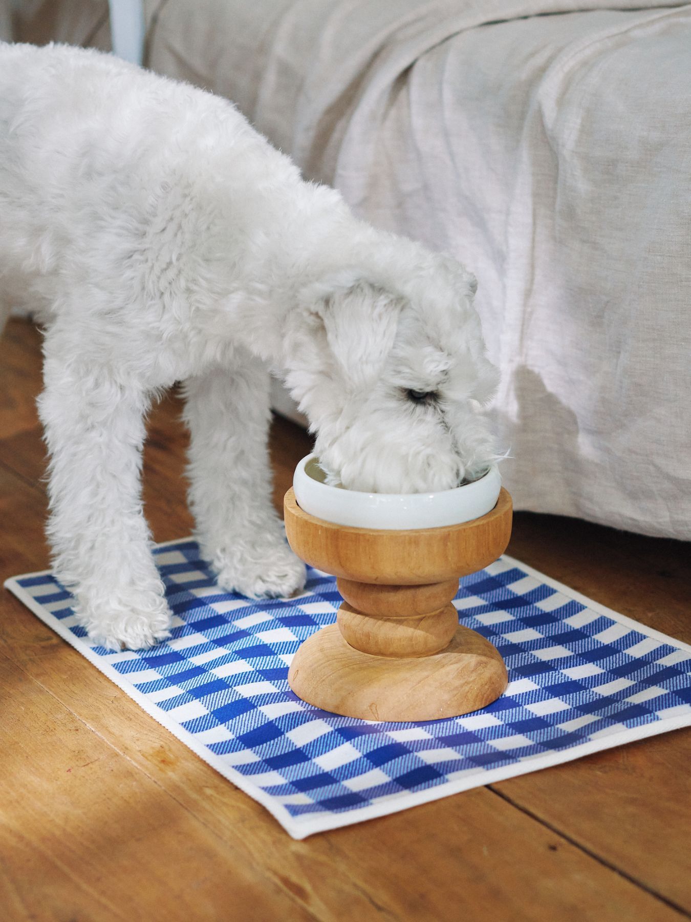 A dog eating from a wooden food bowl on a blue checkered mat.