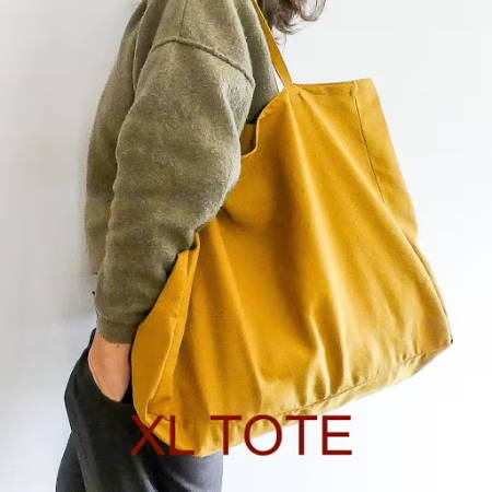 An extra large boxed tote made out of yellow canvas on a women’s shoulder