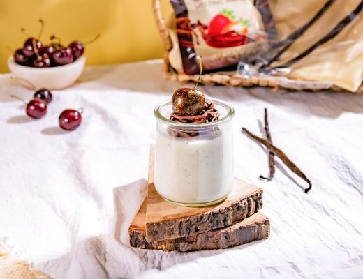 A dessert in a glass jar with toppings, cherries, and vanilla pods.