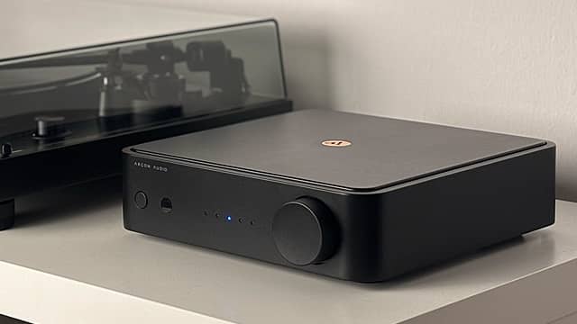 Black audio amplifier next to a turntable on a shelf.