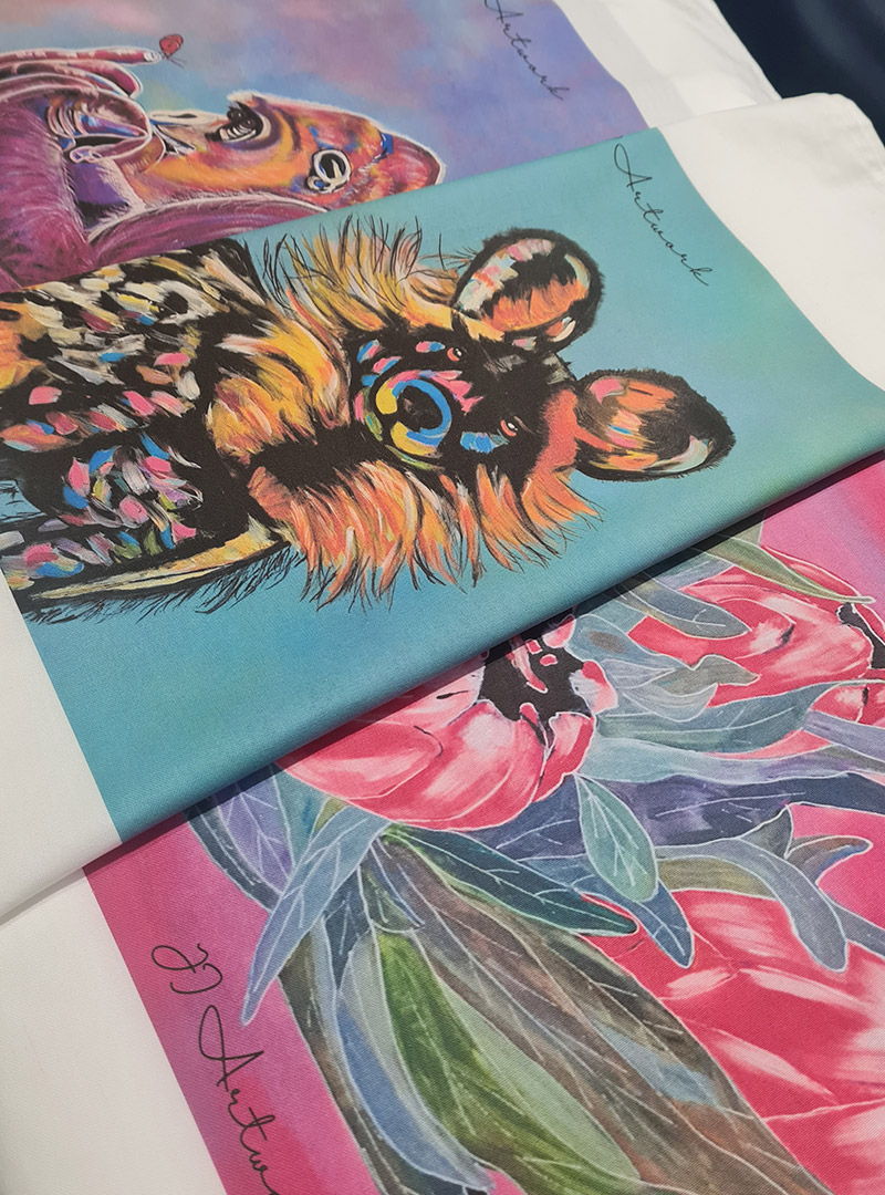 Stack of printed fabrics featuring detailed animal illustrations and painterly artwork with soft brush textures.