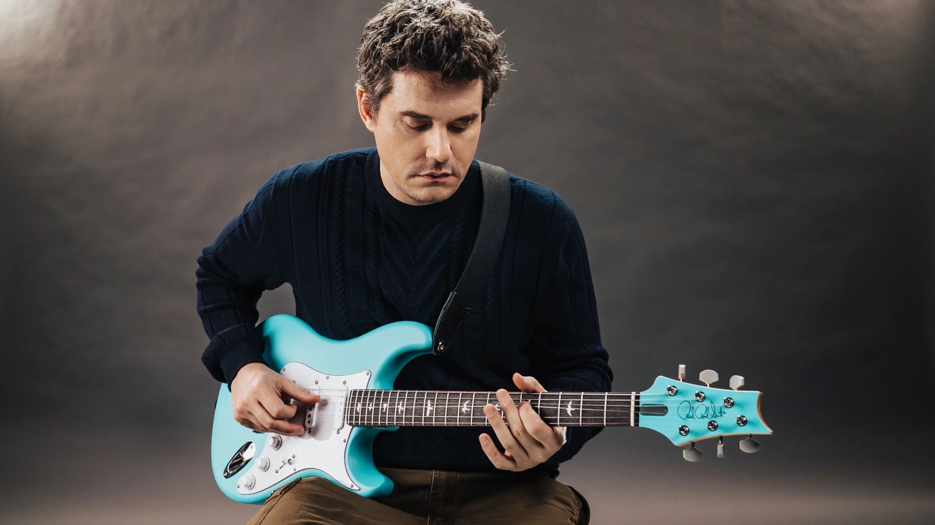 John Mayer playing a light blue PRS Silver Sky guitar against a neutral background.