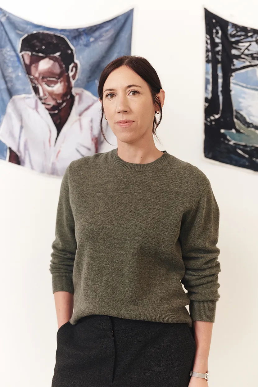 A woman in a sweater stands before two art pieces.