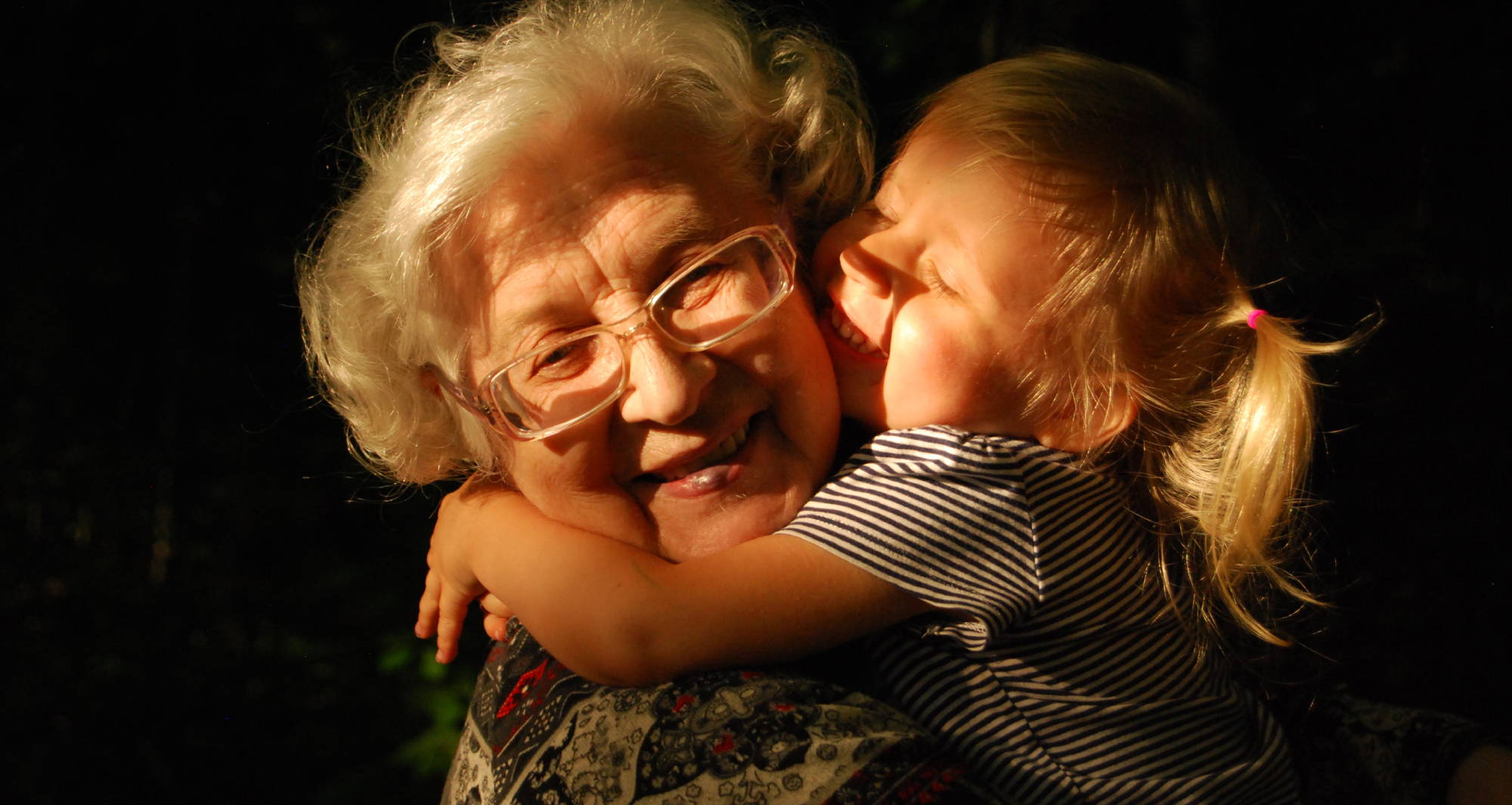  an old lady in glasses hugs a toddler girl