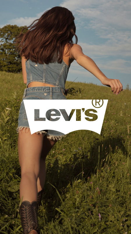 A person walking in a field wearing denim shorts and boots.