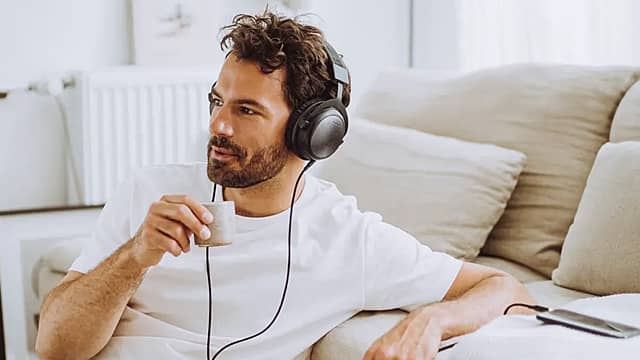 Man wearing wired headphones, sitting on a couch, looking thoughtful.