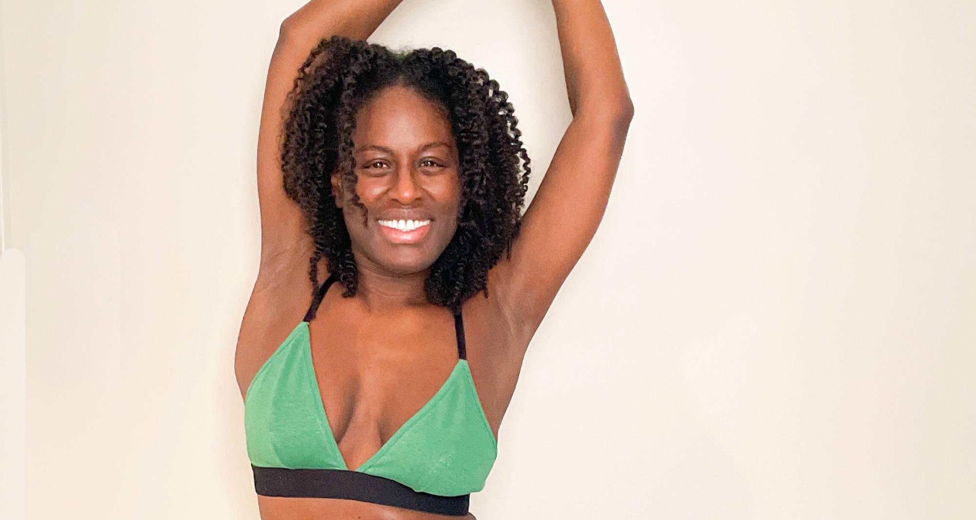 Black woman in green bralette puts her arms above her head.