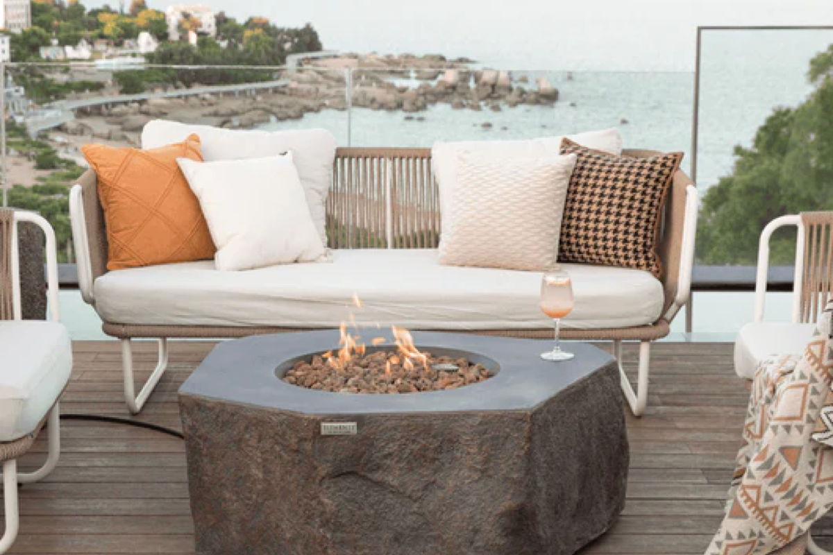 Outdoor fire pit seating area with cushioned sofa, lounge chairs, and coastal water views for a vacation rental patio. 