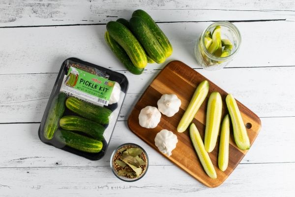 Cucumbers on a cutting board with pickles and a jar of preserves.