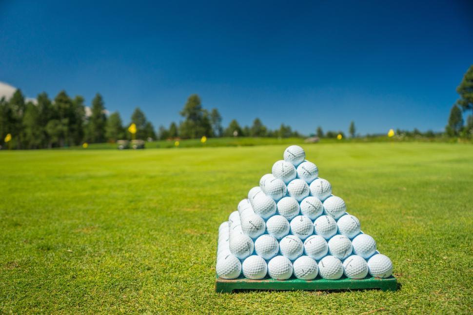 Una piramide di palline da golf su un campo verde sotto un cielo azzurro e limpido.