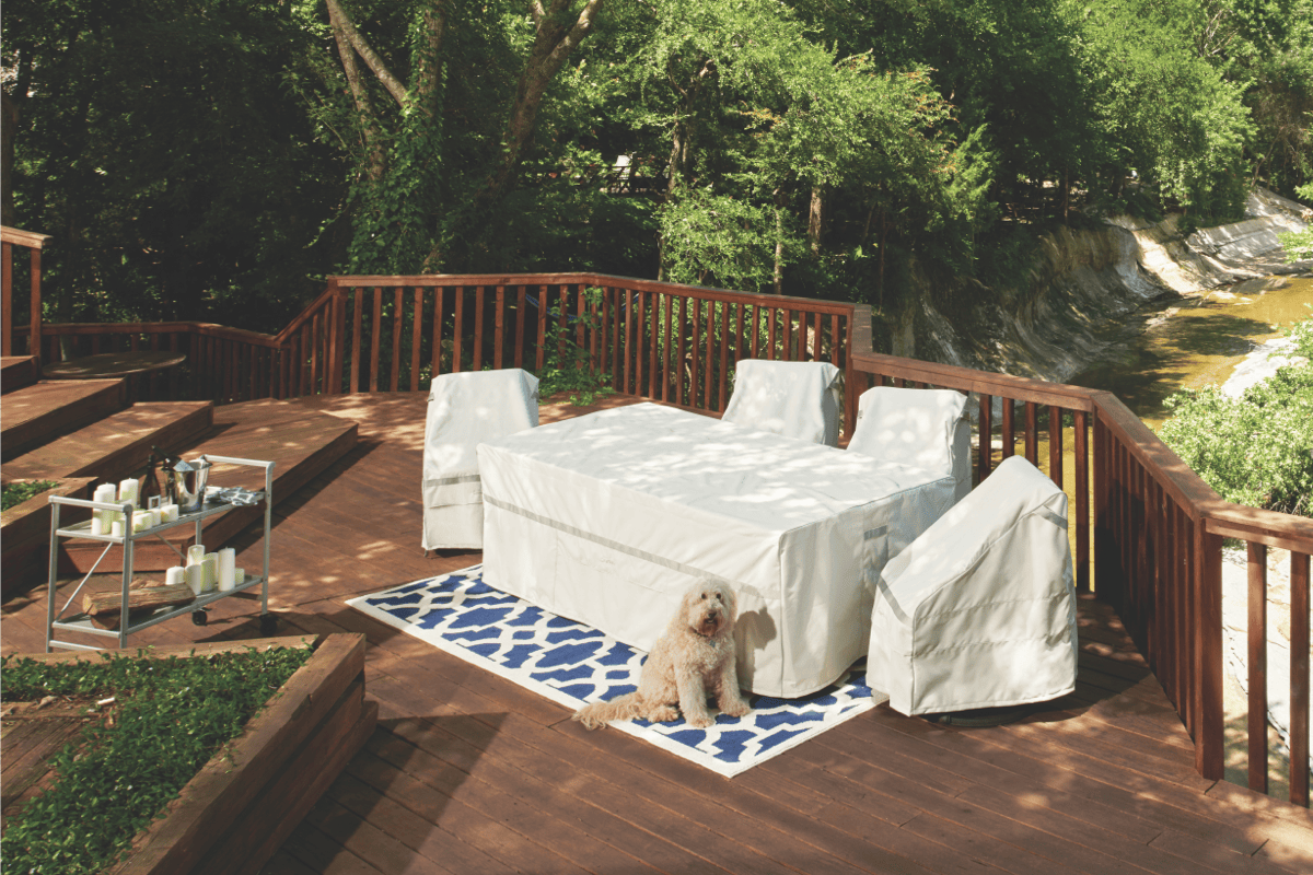 A dog sits in front of a patio dining set protected from the elements with matching covers. 