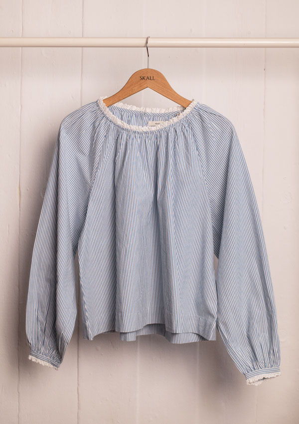 Light blue long-sleeve blouse hanging on a wooden hanger.