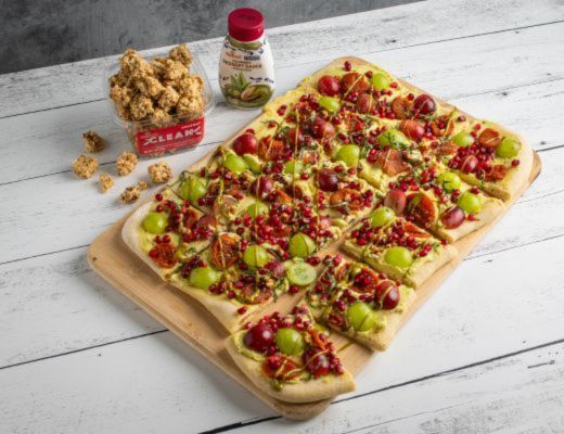 A colorful dessert pizza topped with fruits and nuts on a wooden board.