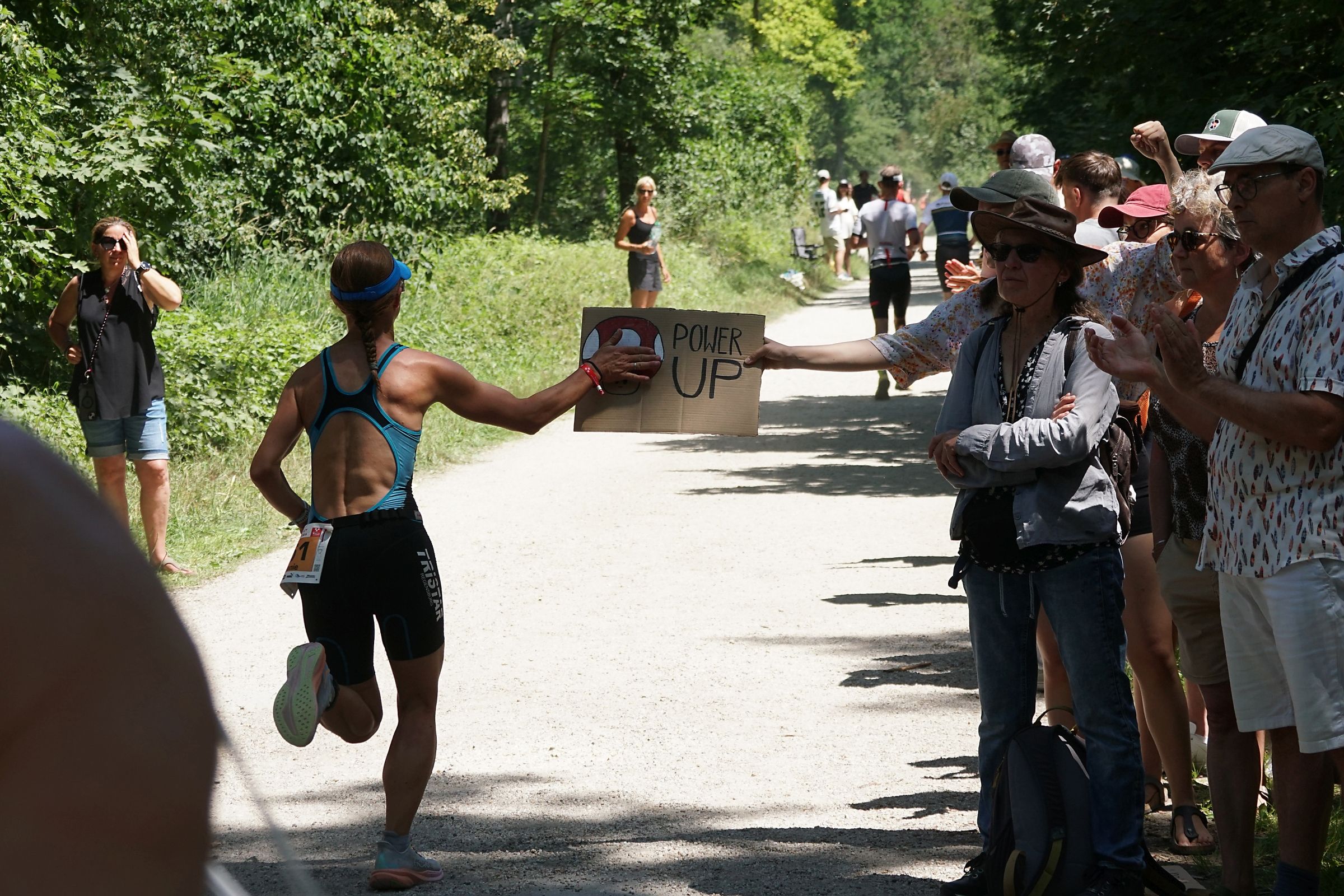 Eine Läuferin wird von Zuschauern am Wegrand der Strecke mit einem Schild angefeuert.