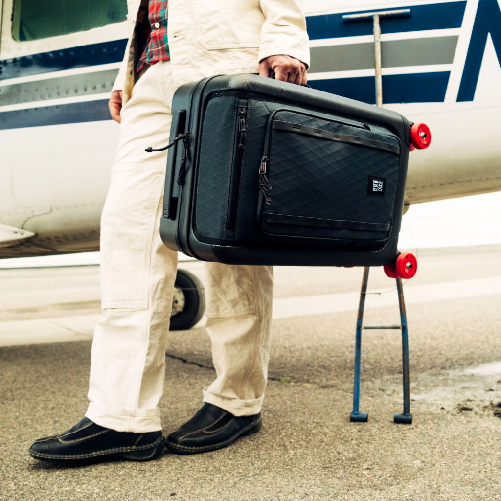 Person holding a black suitcase next to an airplane on the runway.