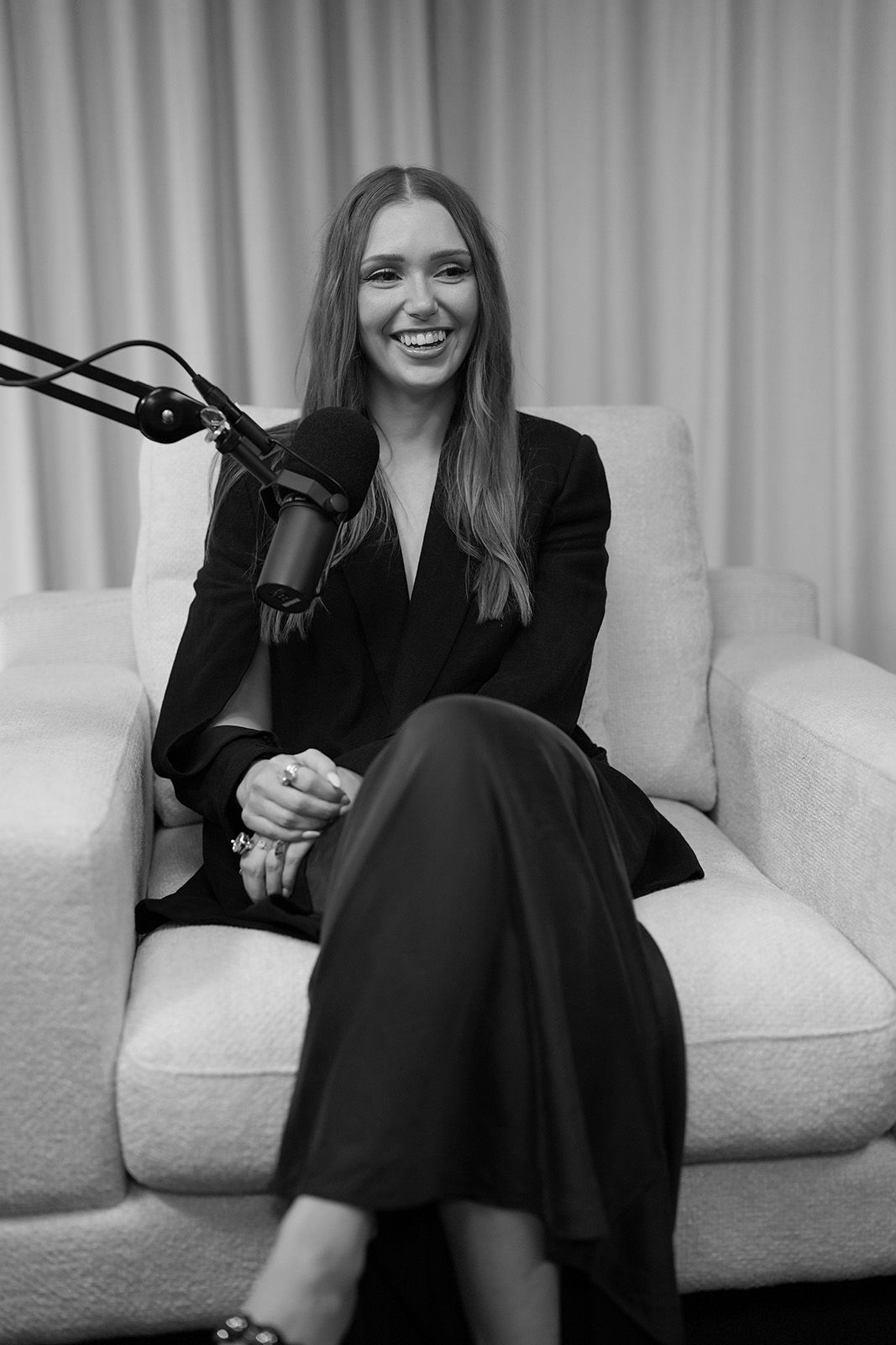 Woman sitting on a couch, smiling, with a microphone nearby.