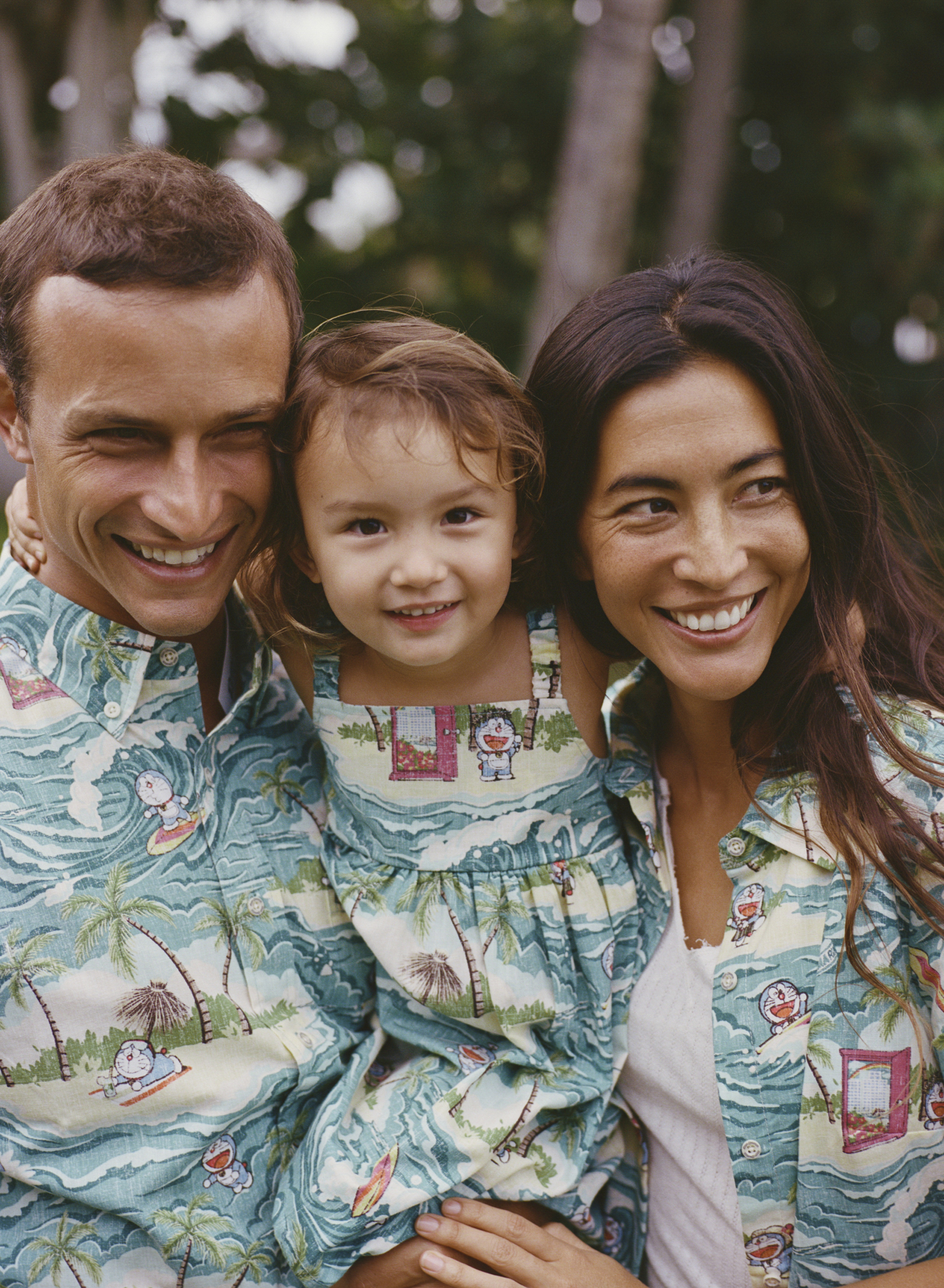 Family smiling together, wearing matching patterned outfits outdoors.