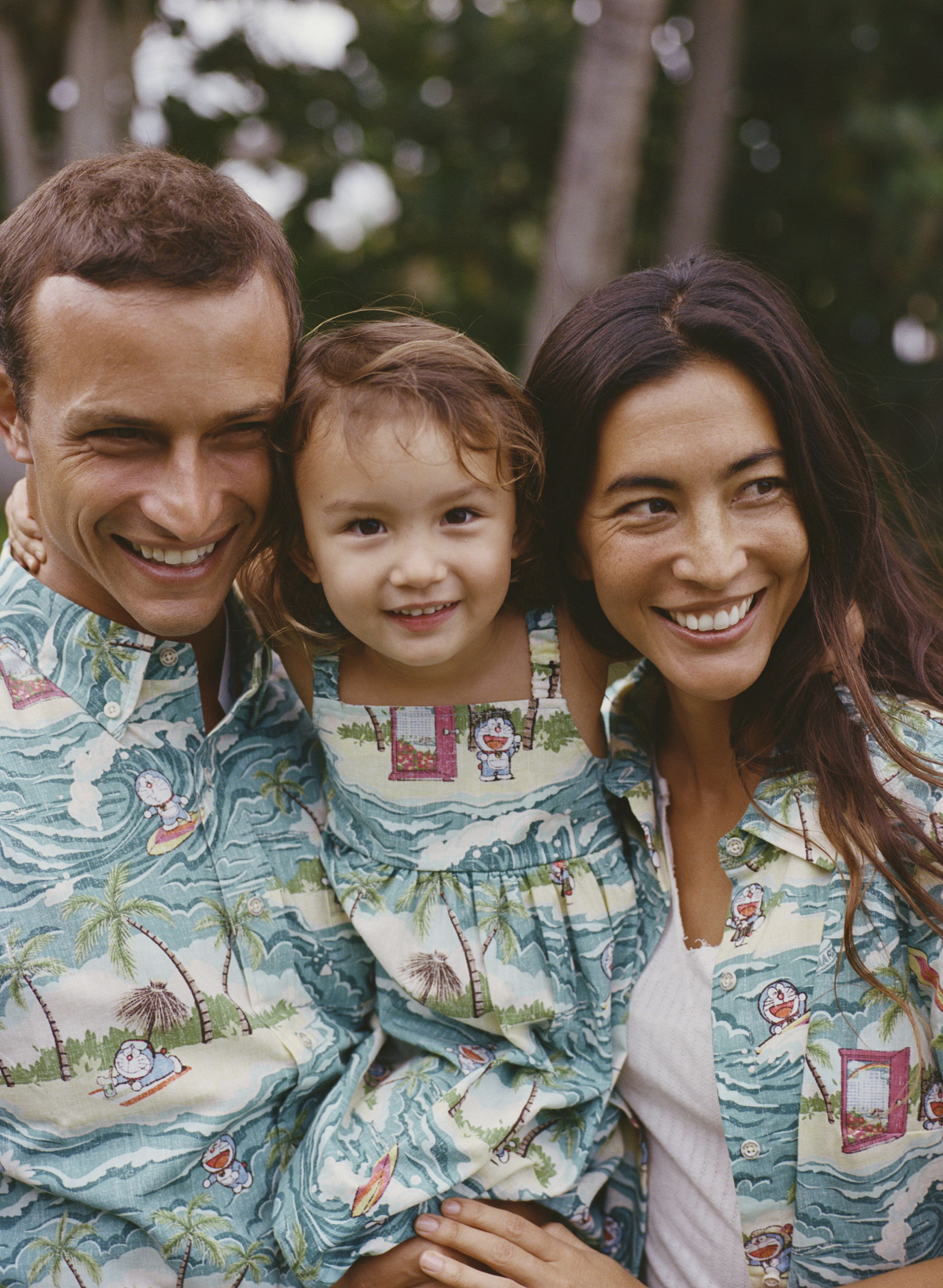 Family smiling together, wearing matching patterned outfits outdoors.