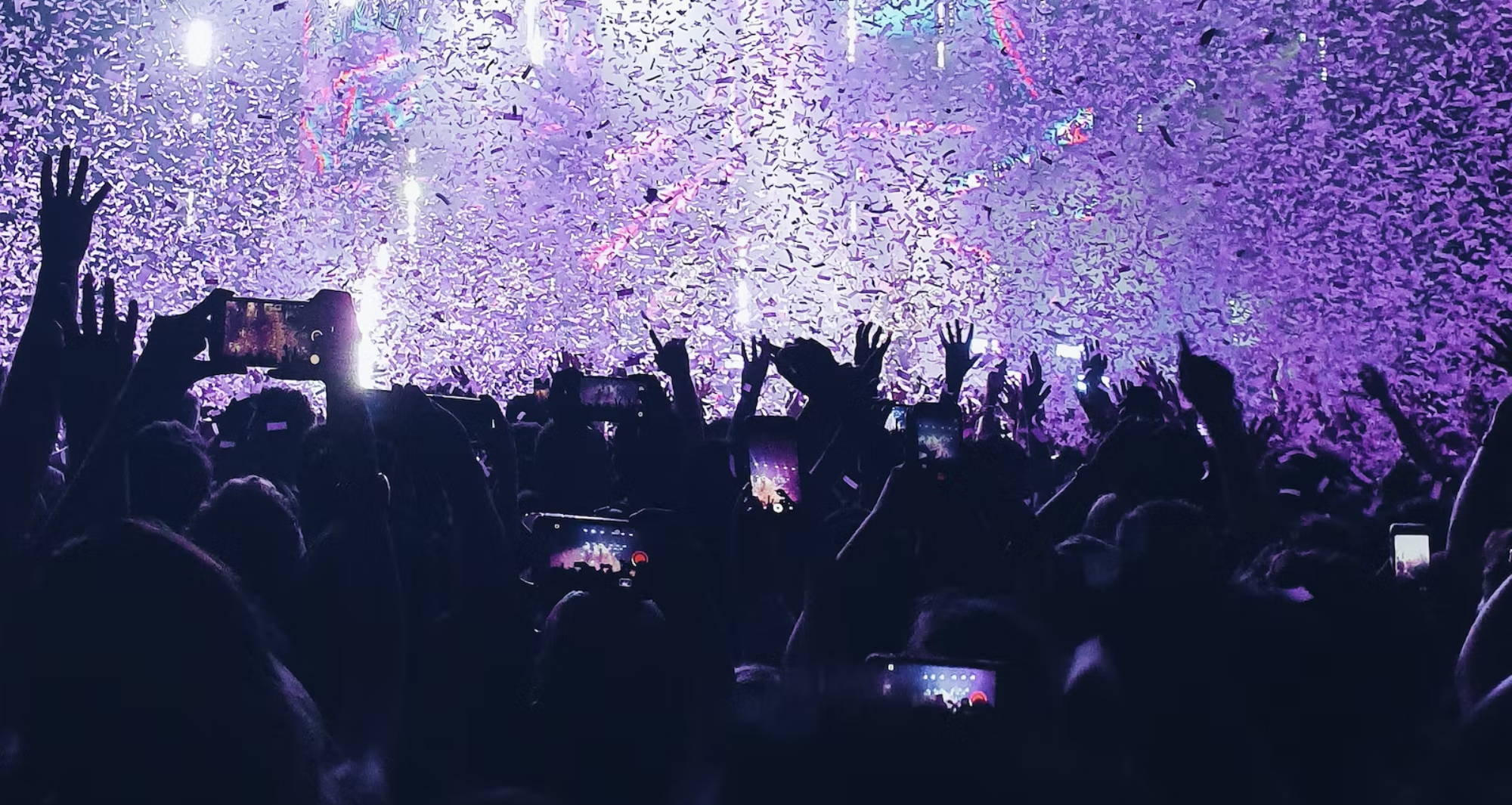  people’s hands in the hair as confetti rains down at a festival