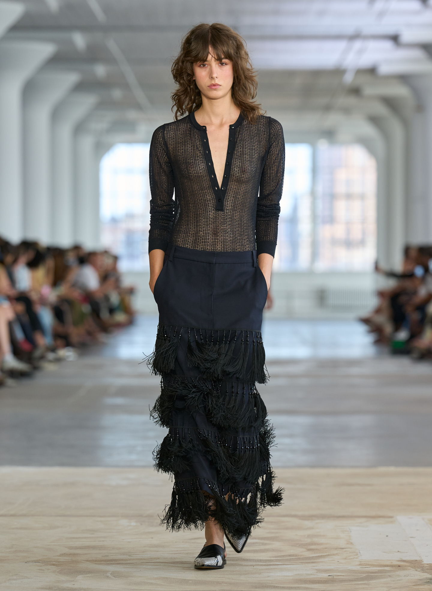 Model walking down runway in black outfit with fringes.
