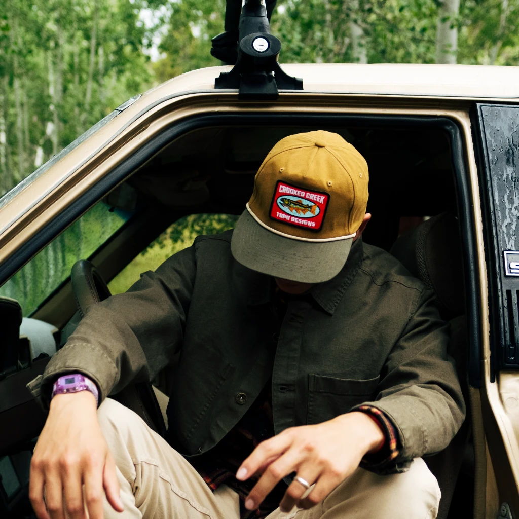 Person in a car wearing a cap and casual clothing, looking down.