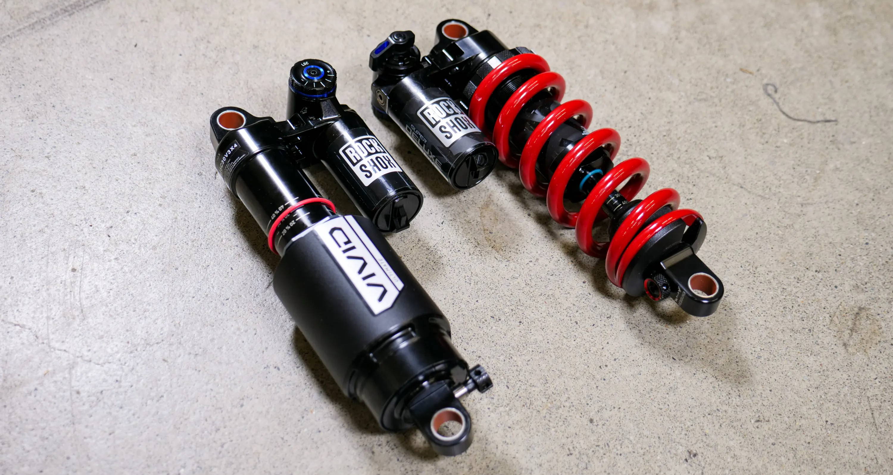 rockshox super deluxe coil ultimate and vivid rear mountain bike shocks laying on concrete to be compared