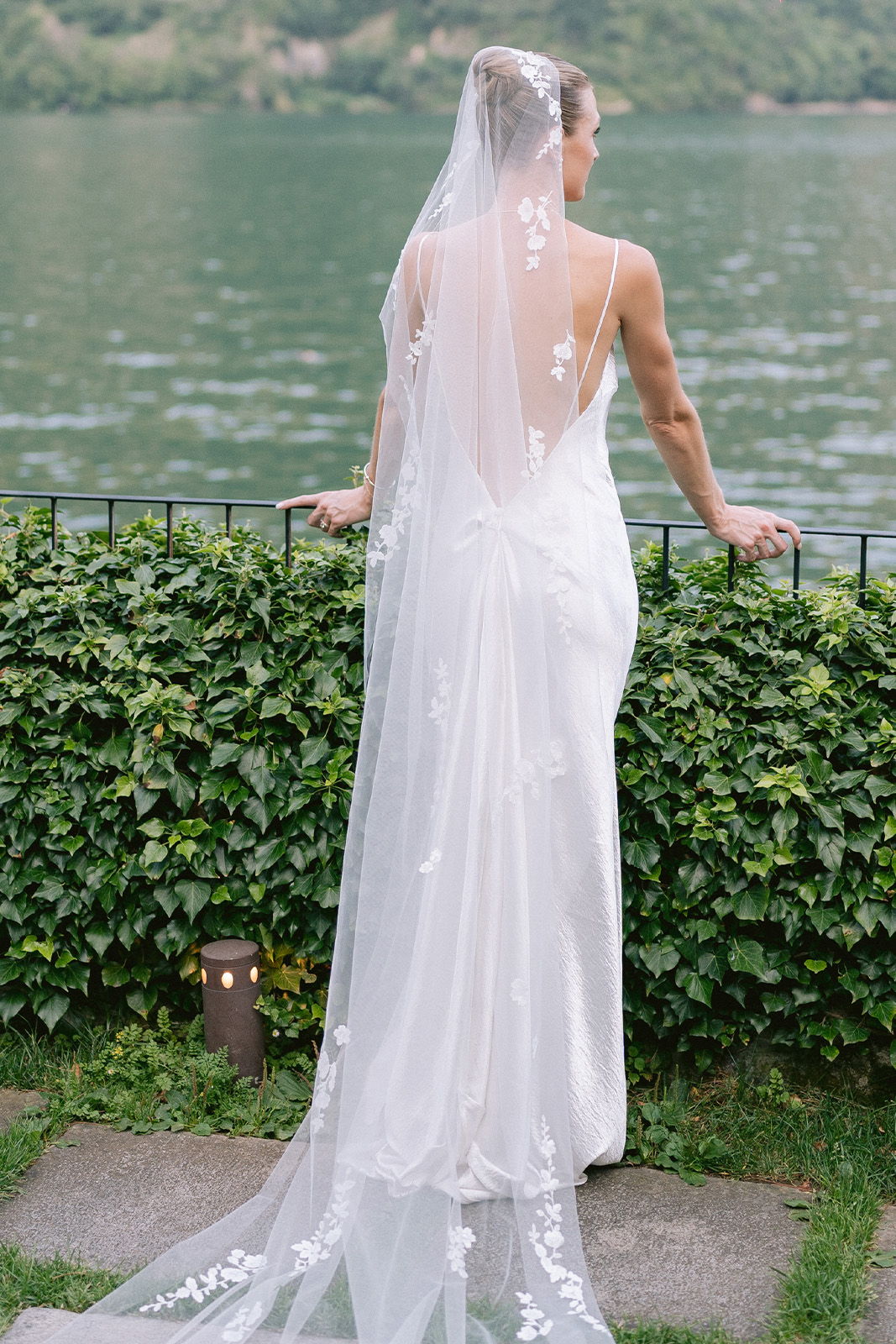 Bride in a white dress and veil by a lake.