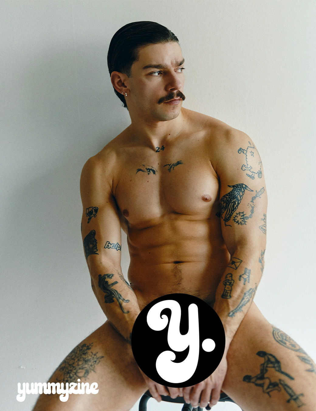 Man with tattoos posing nude, covering lower body with logo.