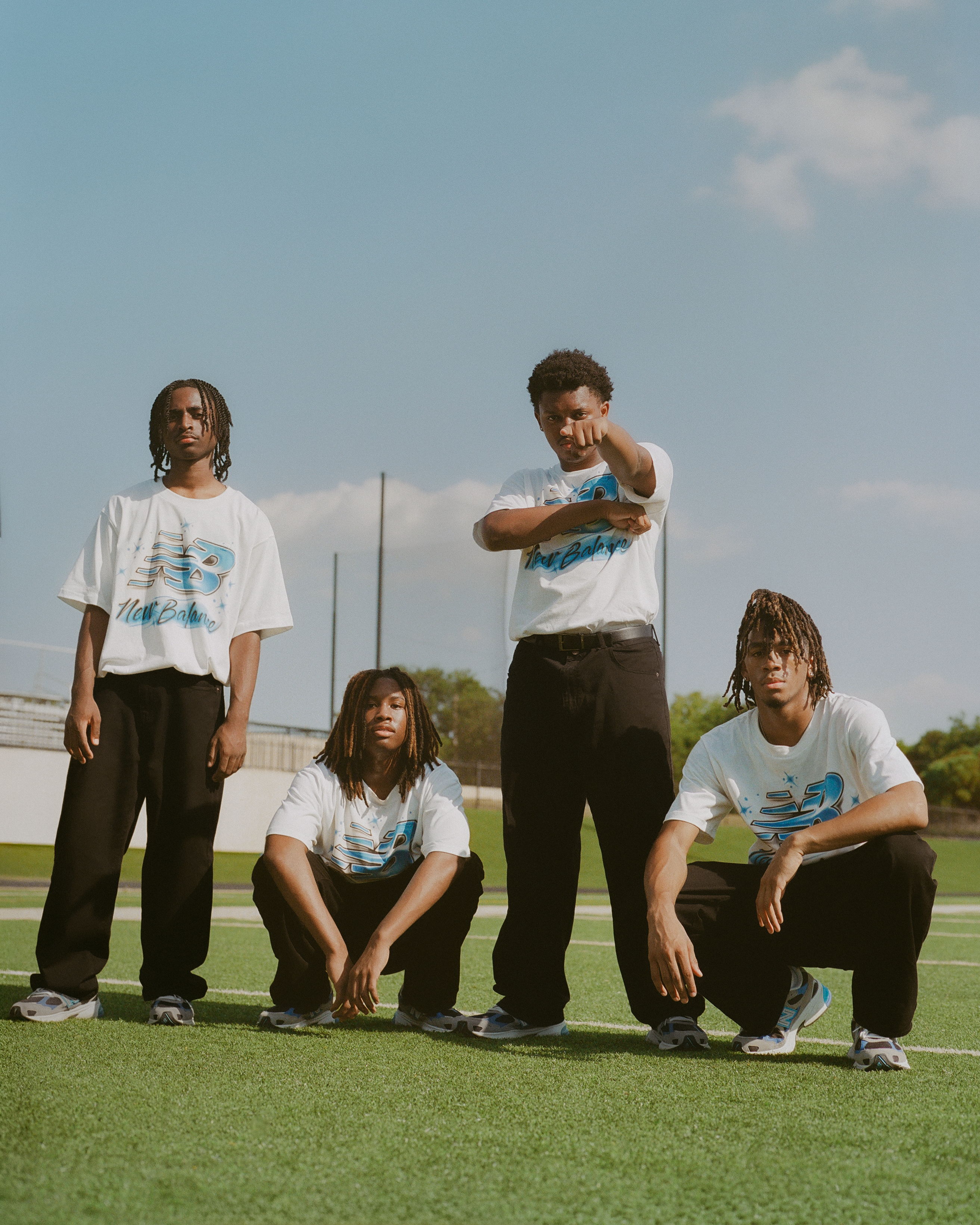 Four individuals in casual attire posing on a sports field.