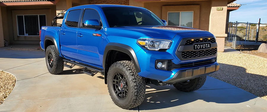 Front three-quarter blue Toyota Tacoma TRD Off-Road TOYOTA heritage grille amber lights black wheels driveway Jeremy's 544K Nightmare Edition featured gallery photo 1