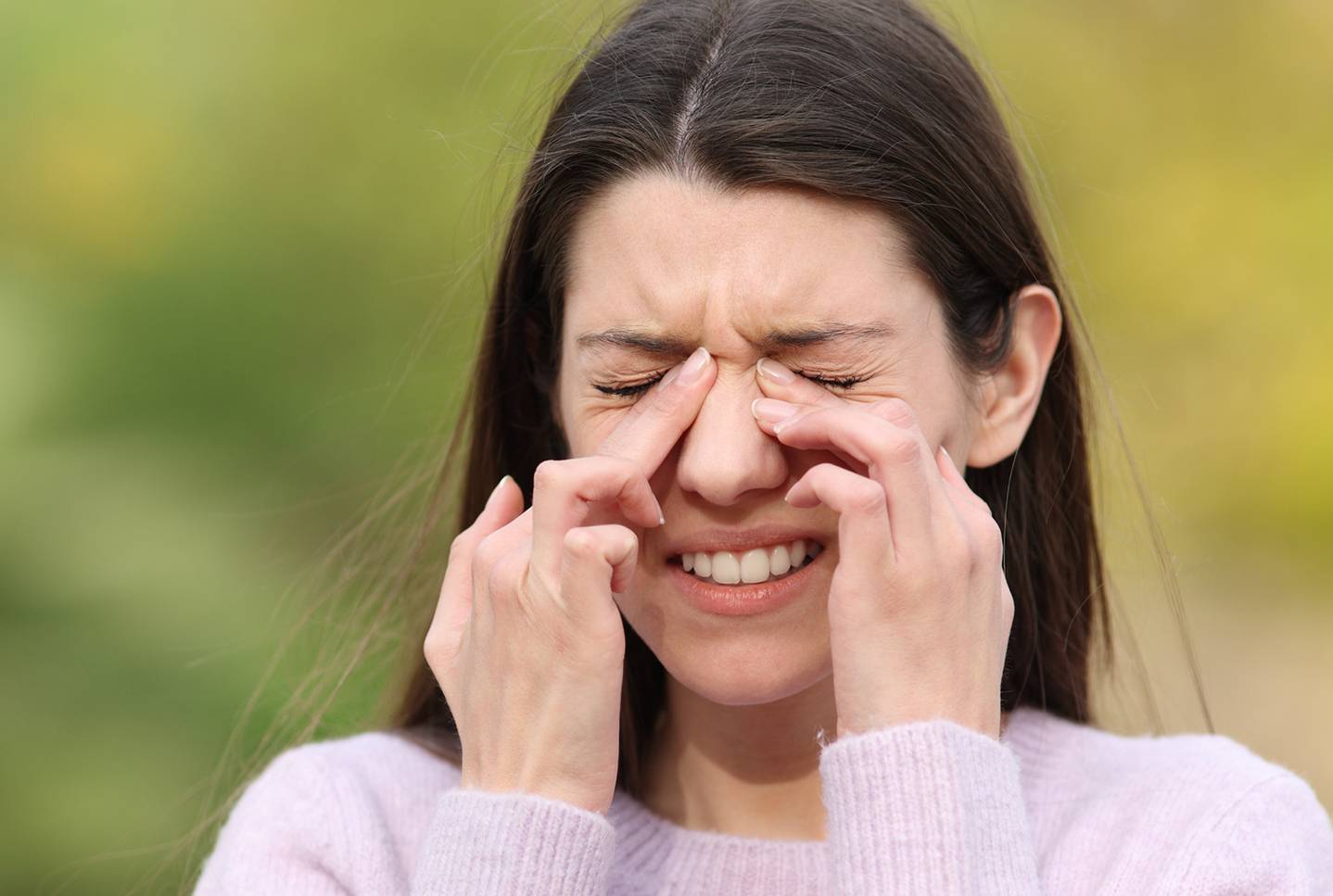 Žena s bolestí si tiskne kořen nosu. Injekce na alergie mohou pomoci zmírnit příznaky alergické rýmy, jako je ucpaný nos.