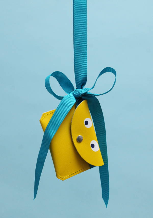 A childrens yellow purse with googly eyes, hanging from a blue ribbon, against a blue background.