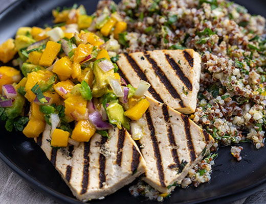 Grilled tofu with mango salsa and quinoa on a black plate.