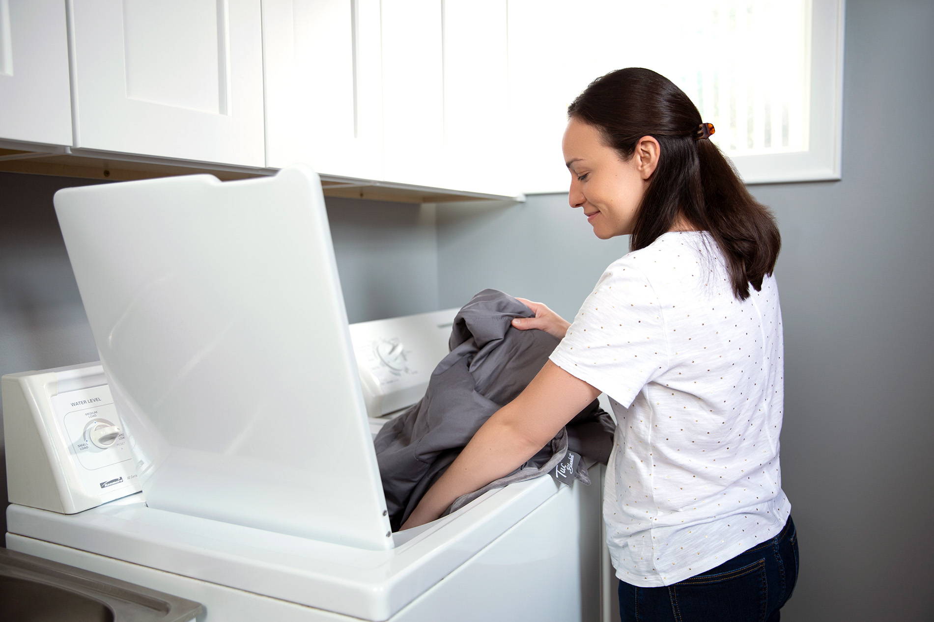 Woman putting a Tuc Kids Cool weighted blanket into the washer.