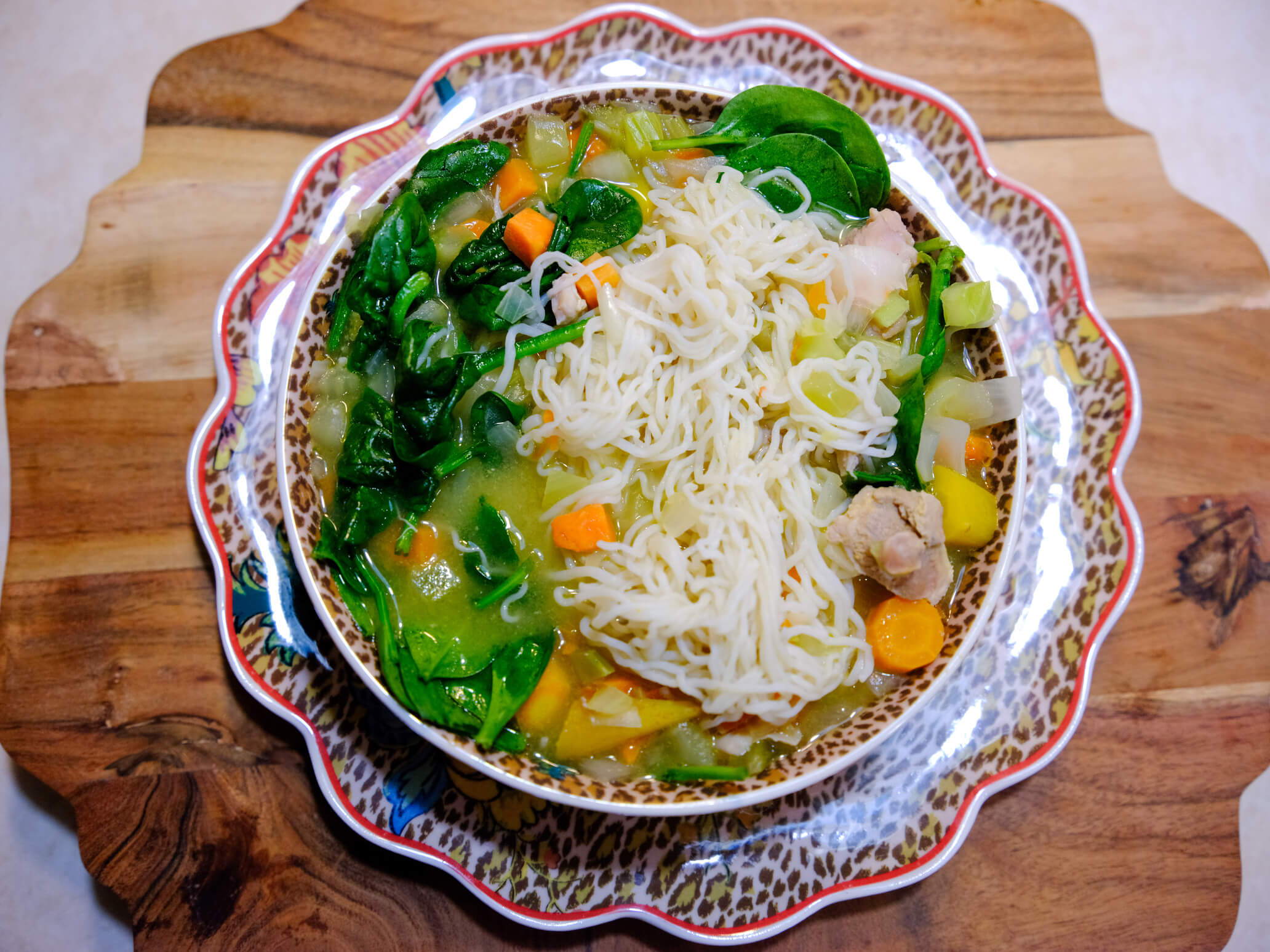 A large bowl full of low-carb Chicken Noodle Soup, made with It's Skinny pasta, spinach, vegetables, and a savory broth.