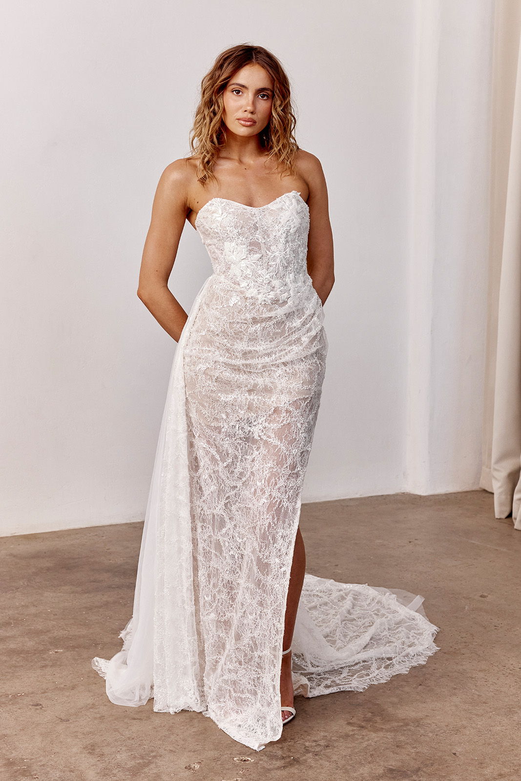 Model wearing a stunning white lace dress with a thigh-high slit.
