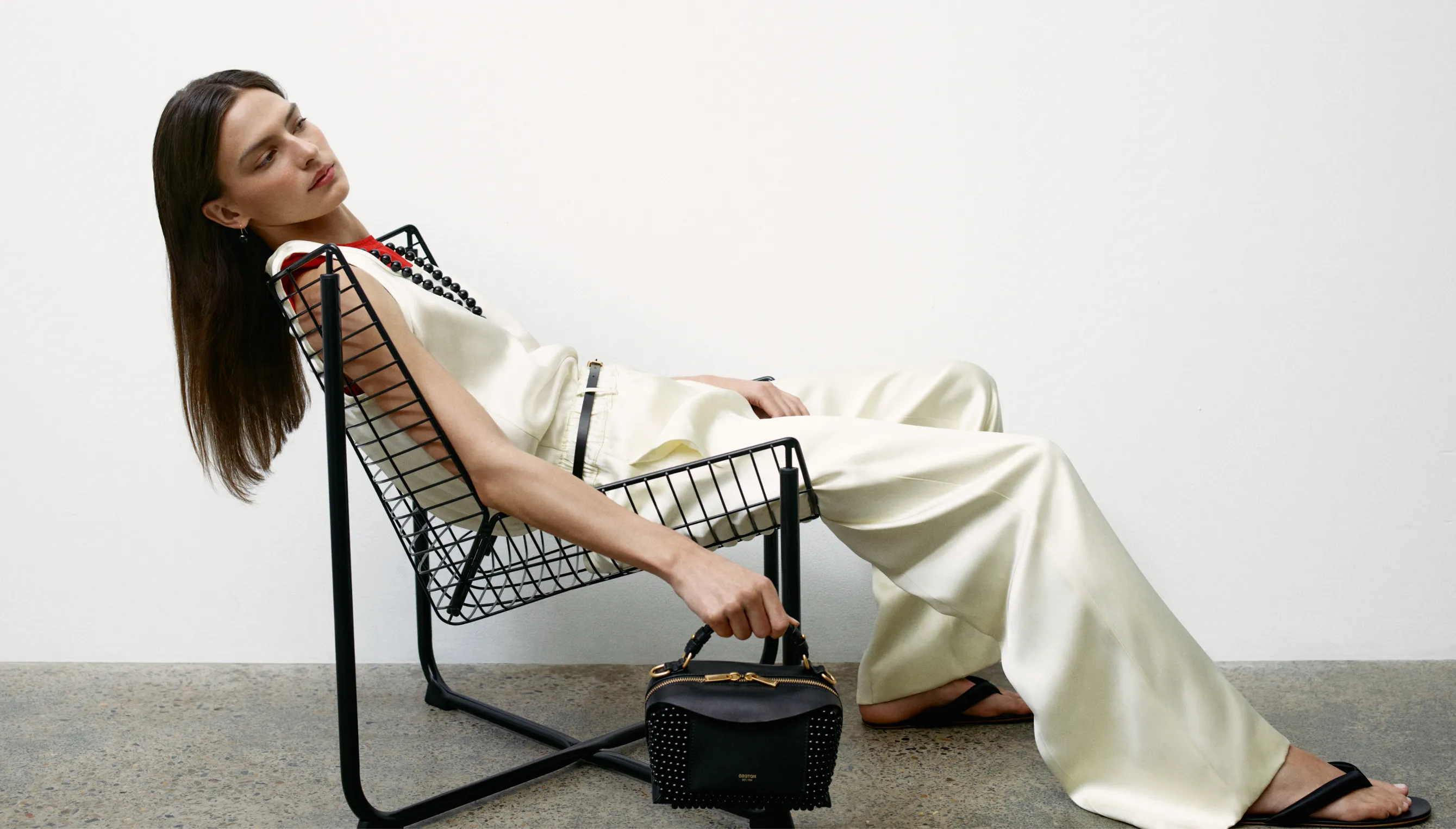 Model in elegant attire lounging on a modern chair with a handbag.