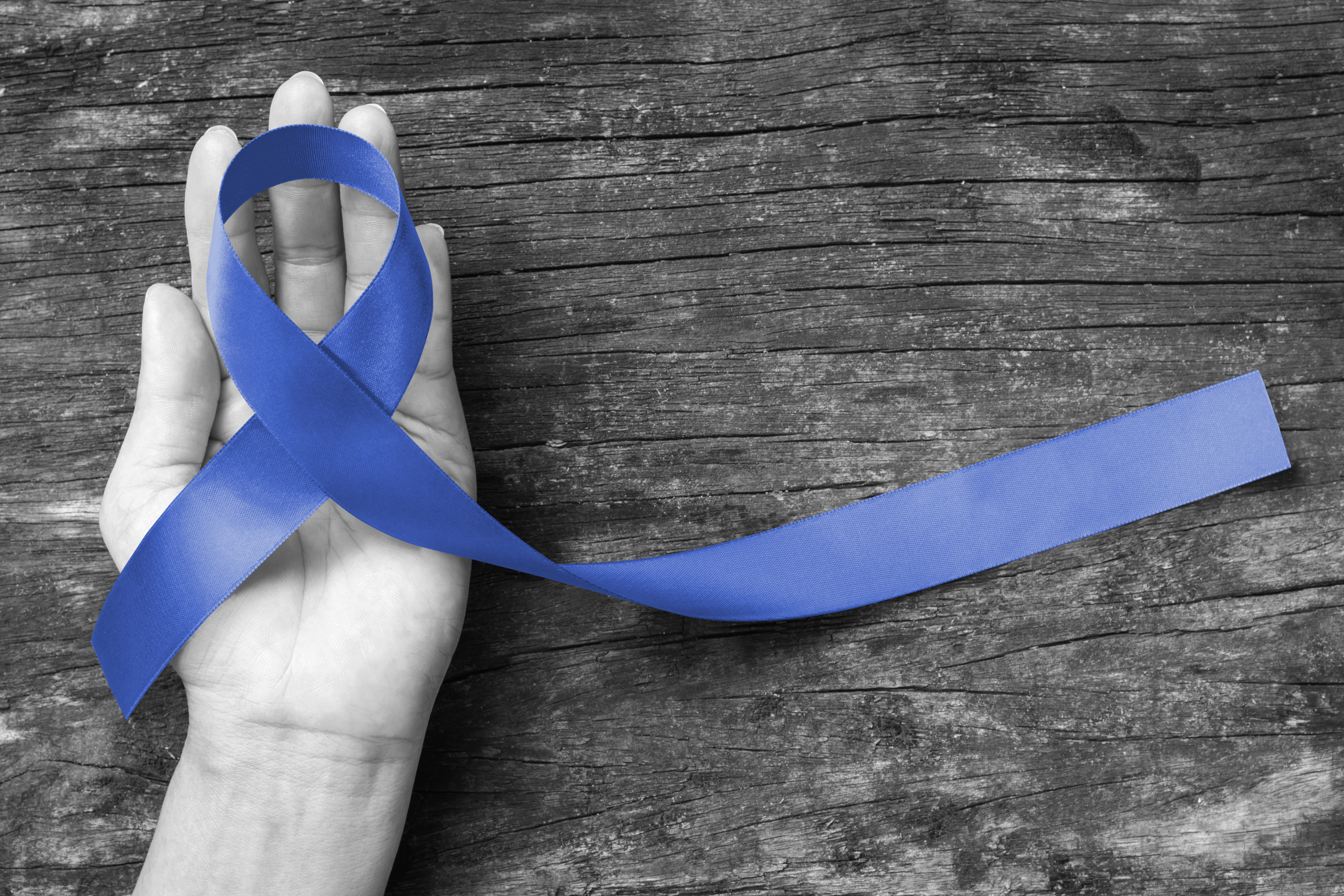 An open hand holding a blue awareness ribbon against weathered wood