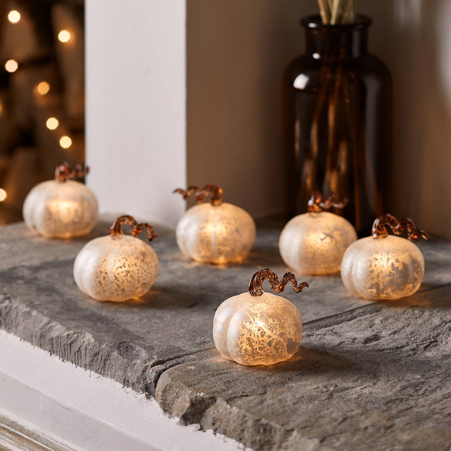6 mini white mottled pumpkins on a fireplace.