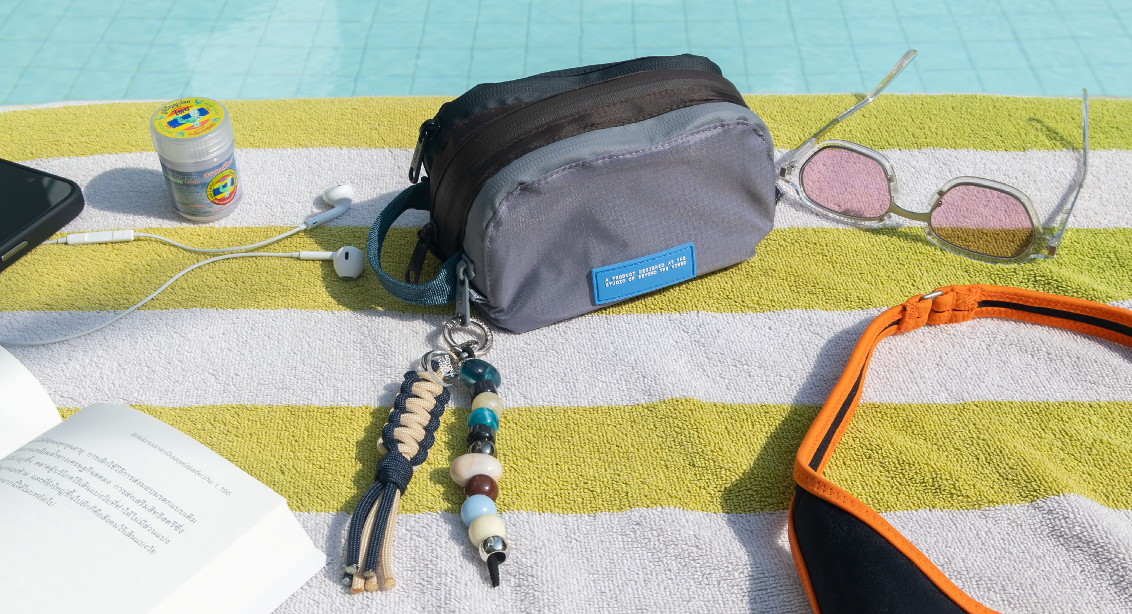 Personal items on a striped towel by a pool, including a bag and sunglasses.