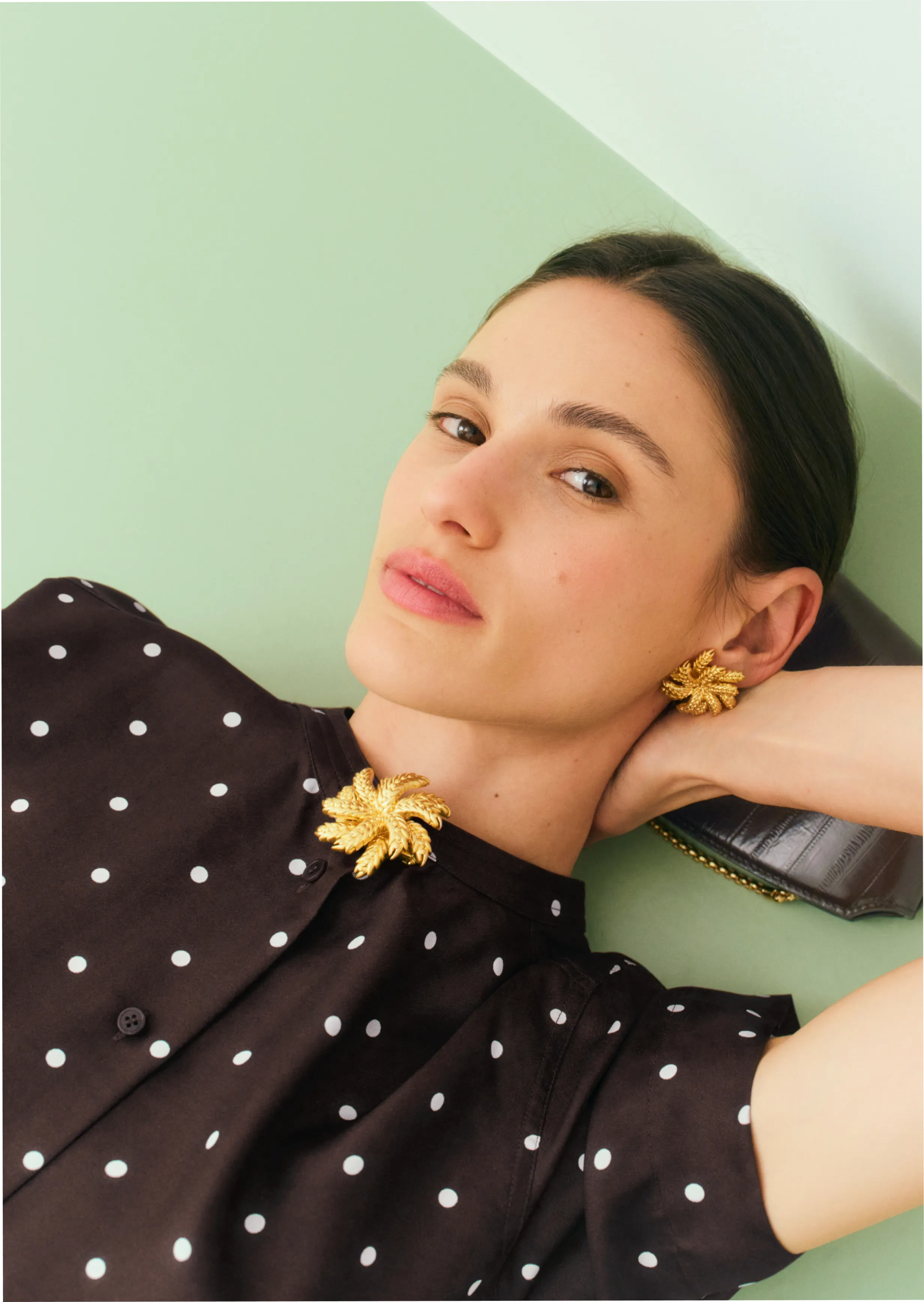 Woman in polka dot shirt with unique jewelry against a pastel background.