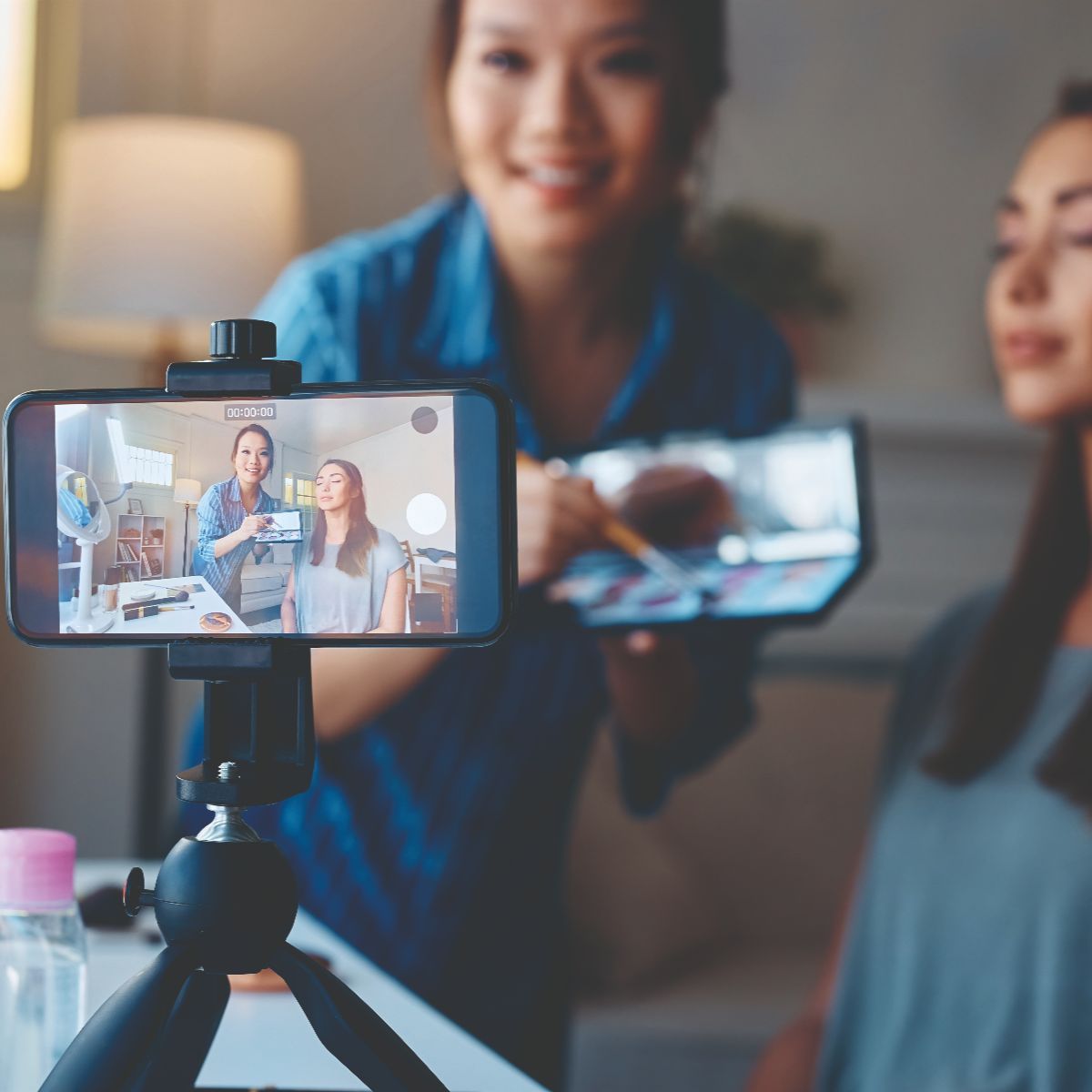 A woman demonstrating makeup application to another woman via video call.