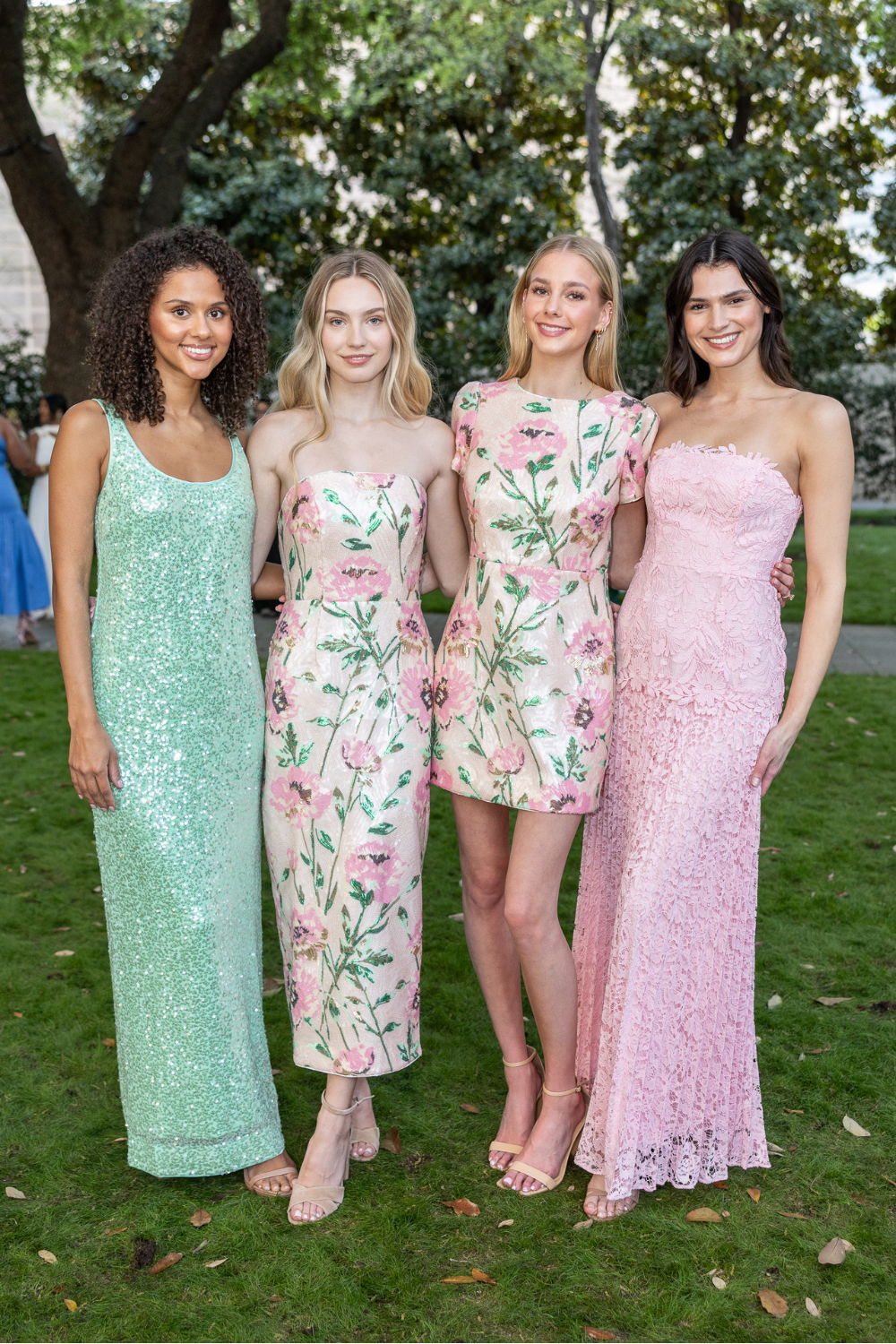 Four models in stylish dresses posed outdoors on grass.