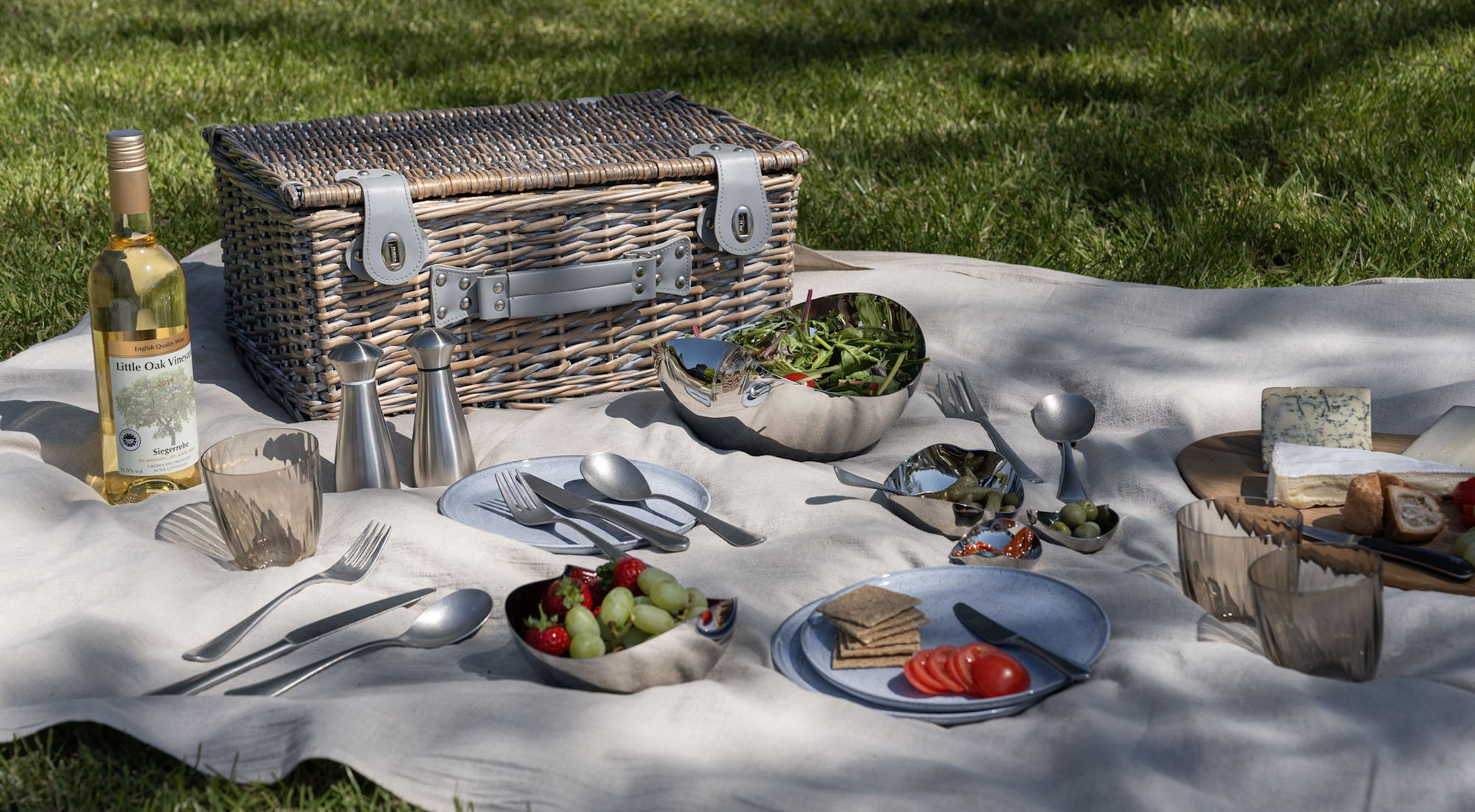 Picnic setup with food, drinks, Robert Welch cutlery, salt and pepper mills, and serving bowls.