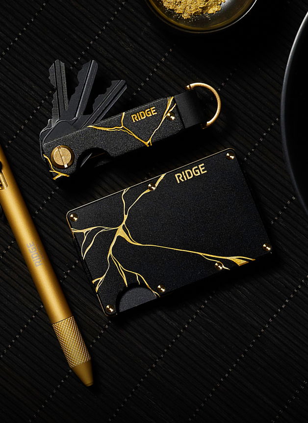 Black wallet and key holder with gold accents on a textured surface.