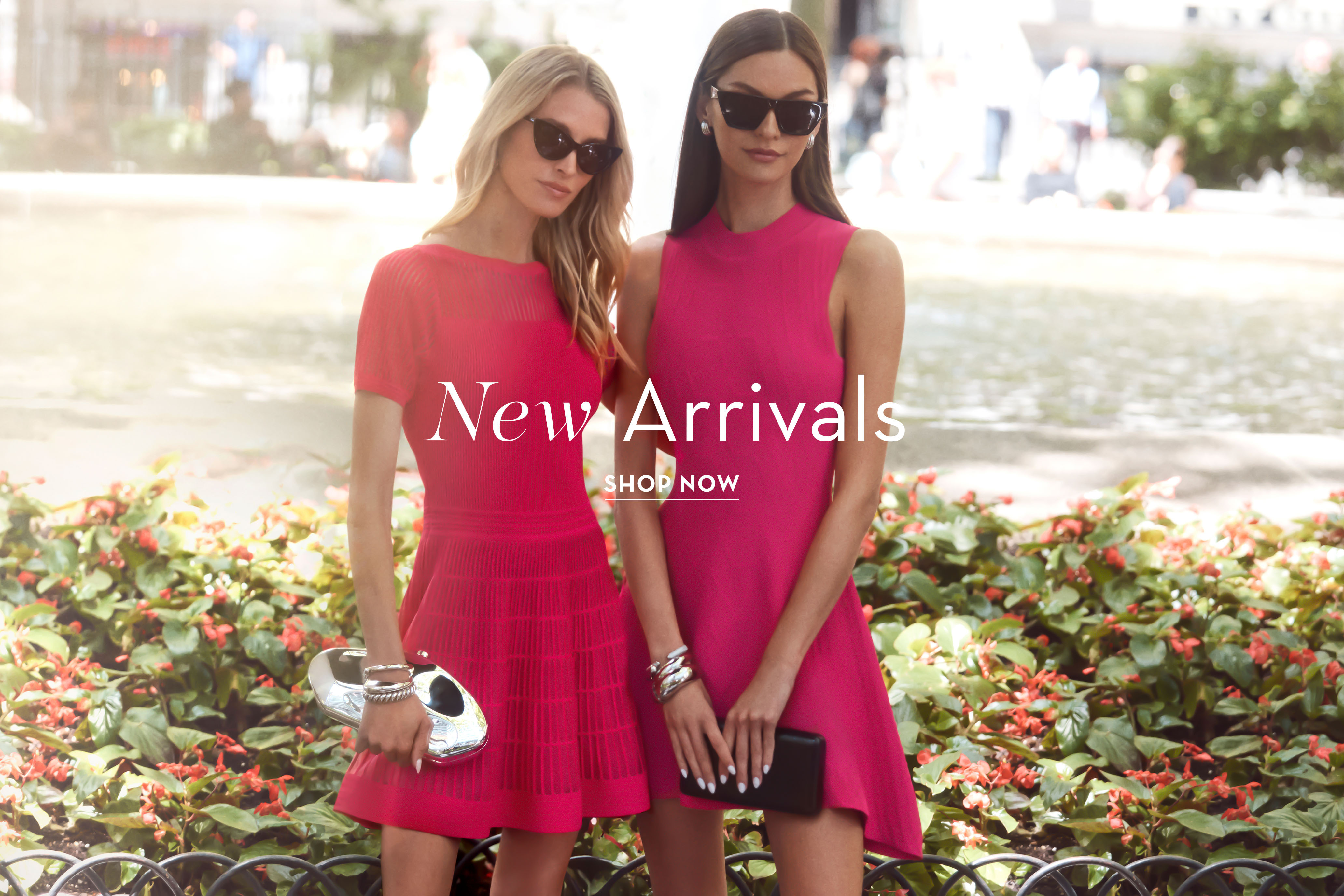 Two women in pink dresses, wearing sunglasses, standing in a garden.
